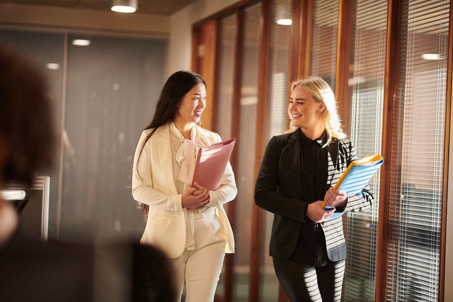 Two confident female attorneys, one Asian and one Caucasian, walk and collaborate in their modern law office. Their positive and focused demeanor represents firm leadership that is free to practice law effectively after optimizing their intake and sales process with the Firm Heartbeat experience.