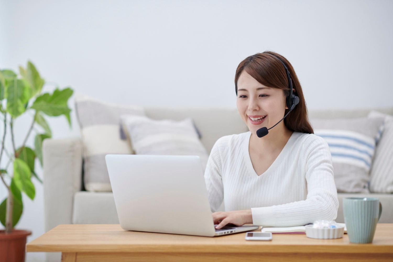 A professional remote intake specialist for a law firm, smiling as she works from her bright home office. She wears a headset and uses a laptop, demonstrating the flexibility and efficiency of a virtual intake system powered by the Firm Heartbeat experience.
