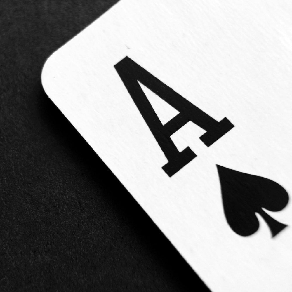 A dramatic, black and white close-up of an Ace of Spades playing card. The powerful card symbolizes the winning competitive advantage—the "ace up your sleeve"—that a professionally repaired intake and sales system from the Firm Heartbeat experience provides to a law firm.