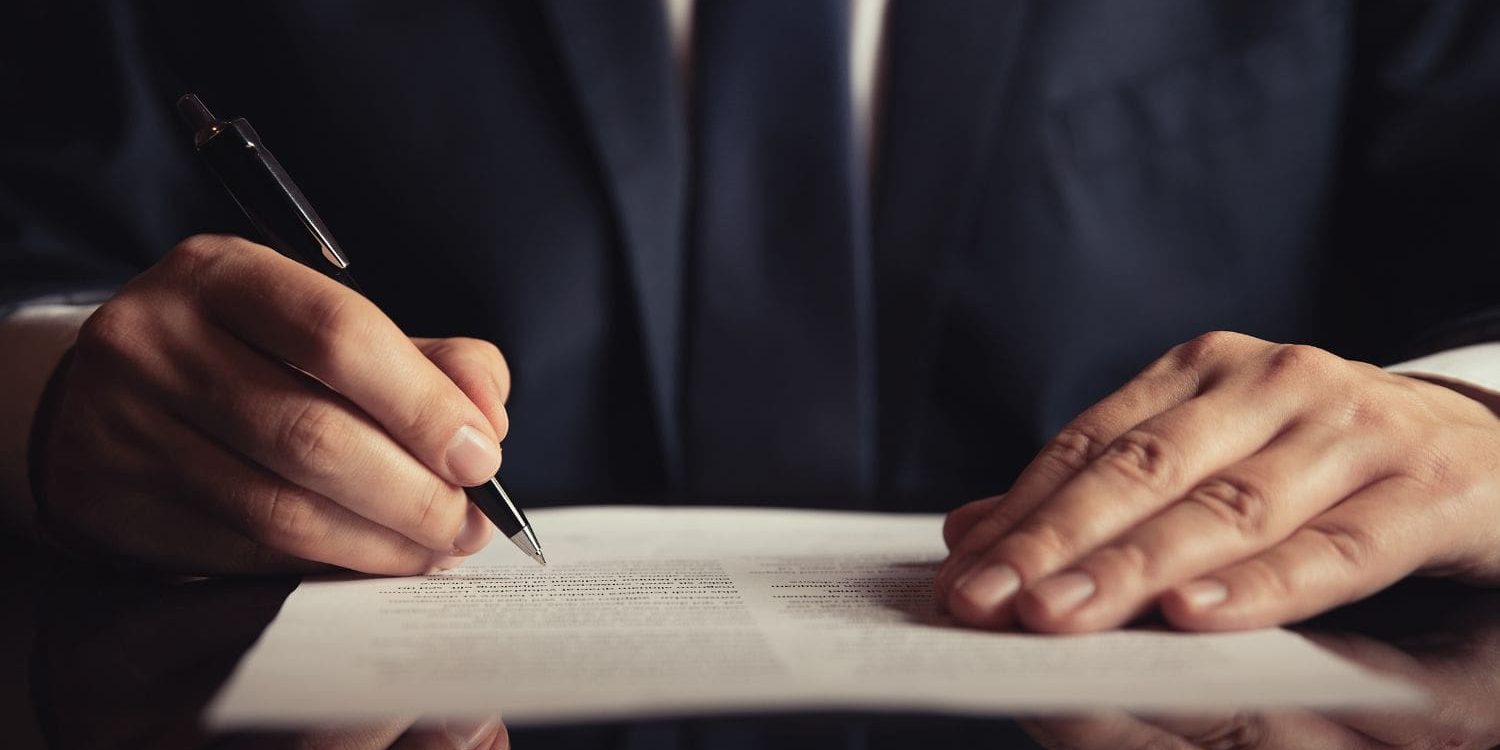 A close-up, professional shot of a person in a business suit signing a legal contract, symbolizing the final moment of client conversion. This act of commitment represents the successful outcome of the streamlined intake and sales process built by the Firm Heartbeat experience.