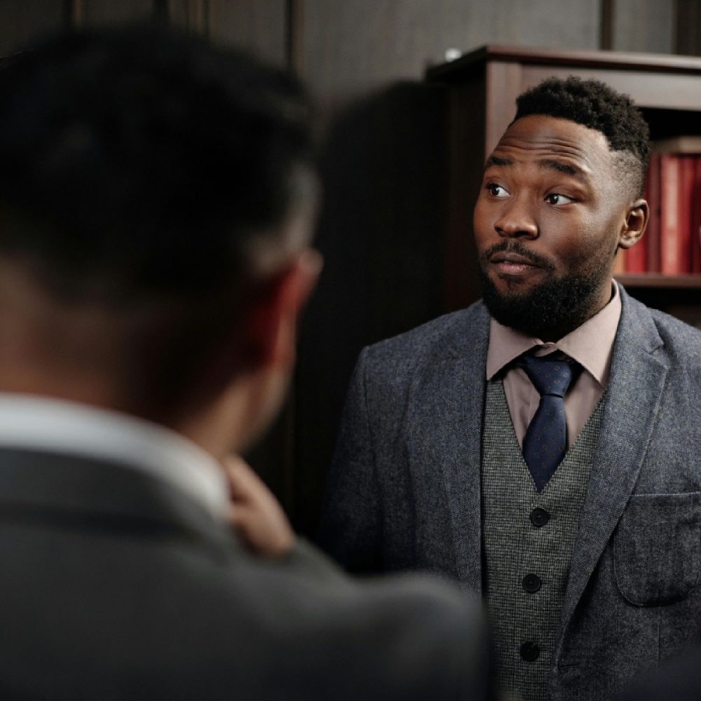 Two male attorneys in a serious, private conversation within a classic, wood-paneled law office. The concerned and attentive expression on the man in focus, a Black attorney in a tweed suit, represents the moment firm leadership confronts a critical business challenge, such as a failing intake and sales process, which the Firm Heartbeat experience is designed to solve.