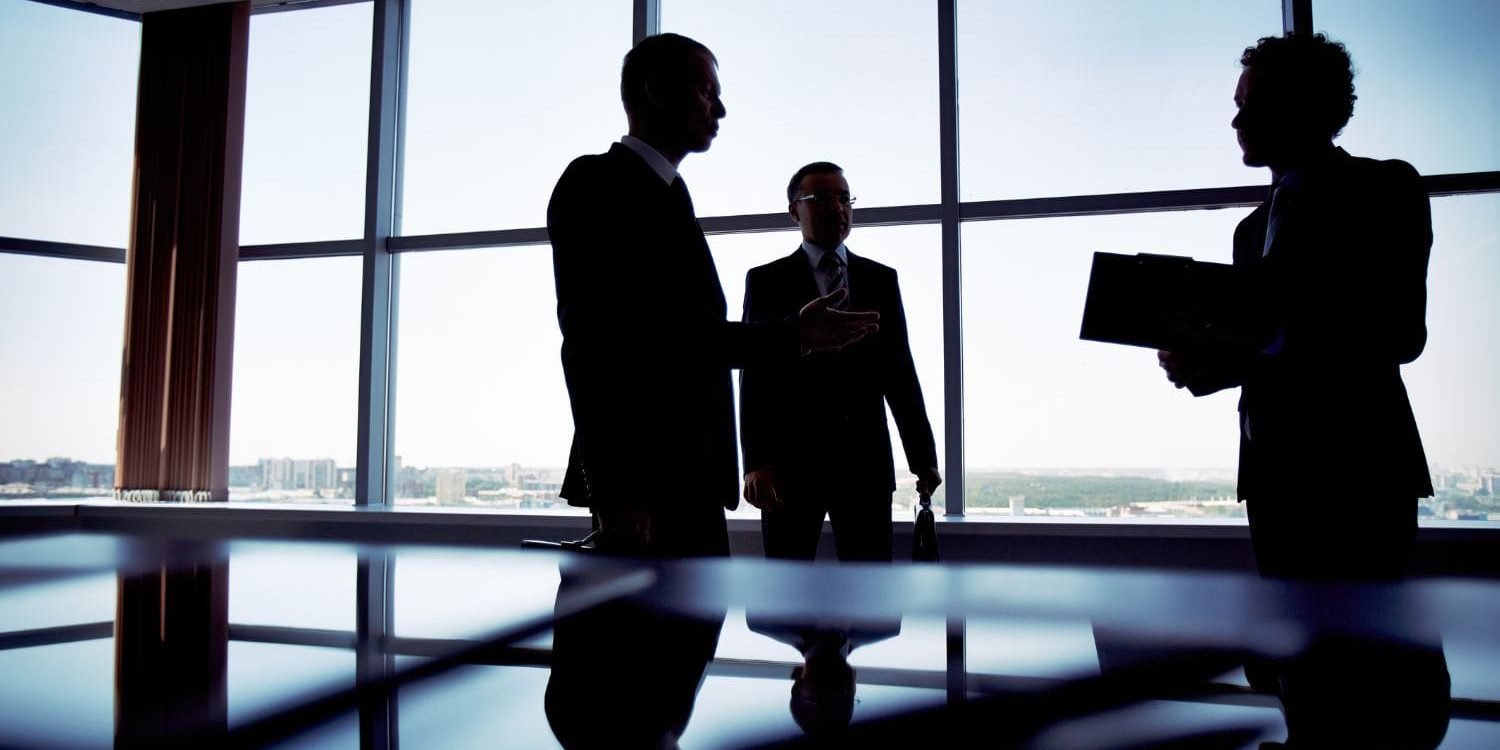 The silhouettes of three law firm partners engaged in a high-stakes strategic meeting in a modern, high-rise conference room. This represents the top-level focus that firm leadership can achieve once their client intake and sales systems are optimized by the Firm Heartbeat experience.
