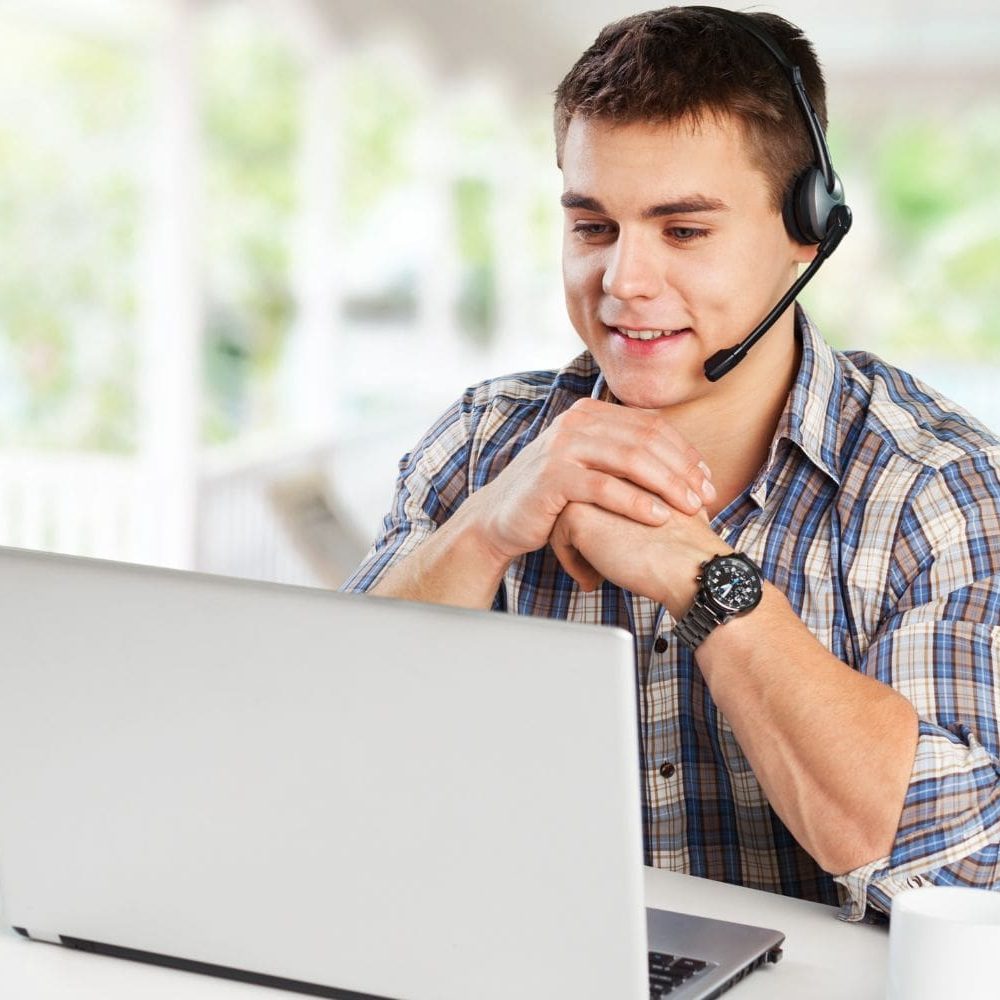 A professional male intake specialist wearing a headset sits at his desk, attentively engaging with a potential client on his laptop. He has a positive, focused expression, representing an efficient and successful law firm client intake process implemented by Firm Heartbeat.